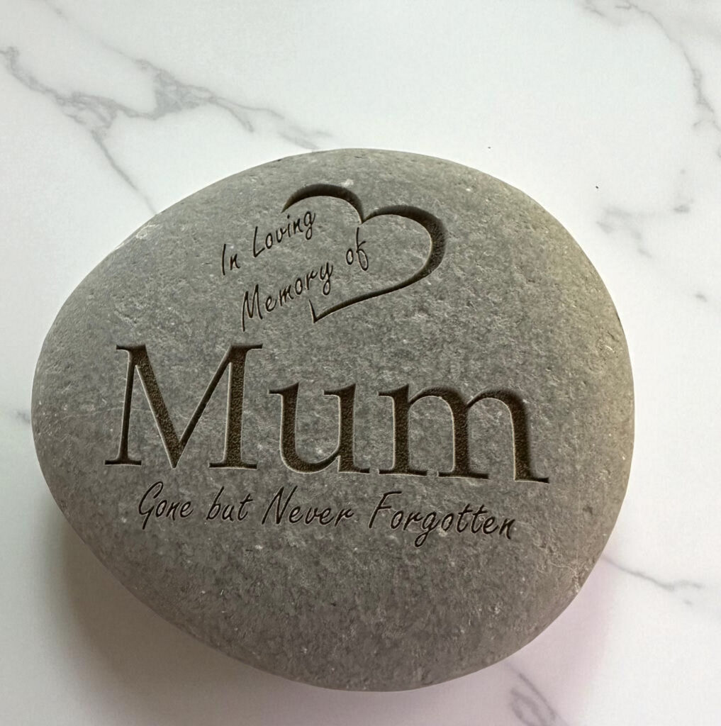A grey memorial stone engraved with the words 'In Loving Memory of Mum' and 'Gone but Never Forgotten' alongside a heart design.